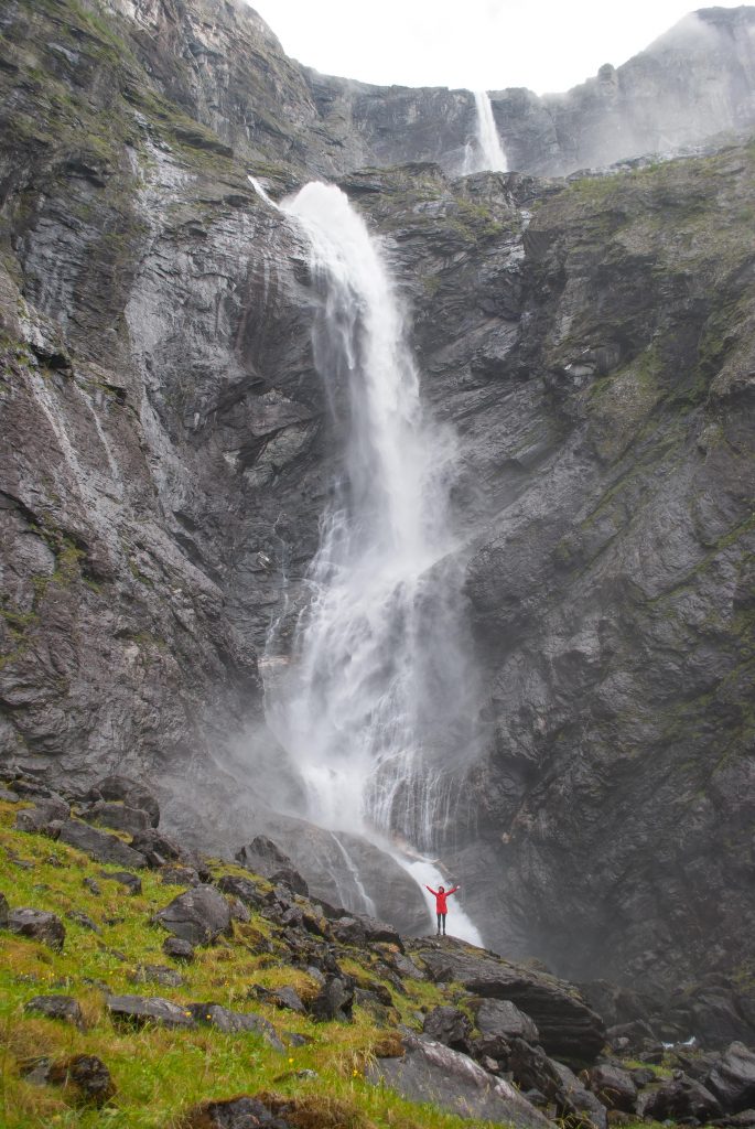 Vrouw in rode regenjas bij de gigantische Mardalsfossen waterval in Noorwegen